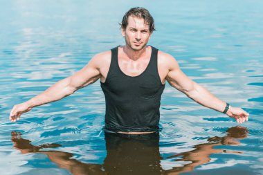 Sudaki yakışıklı adam, kaslı fit vücut gösteren seksi adam. Spor hayatı kavramı. Güneşli bir günde kumsalda kaslı bir erkek vücudu.