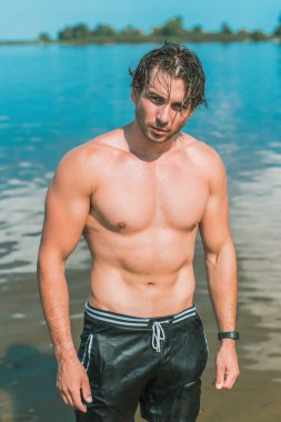 Sudaki yakışıklı adam, kaslı fit vücut gösteren seksi adam. Spor hayatı kavramı. Güneşli bir günde kumsalda kaslı bir erkek vücudu.