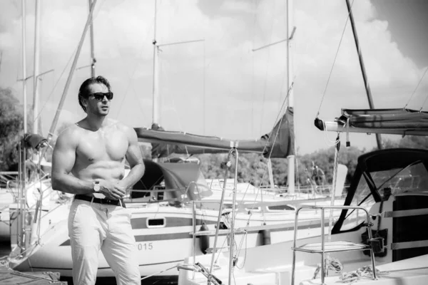 Sexy bearded man standing on the yacht club. Guy on a sailing boat. Handsome man enjoying life, traveling on yacht along beautiful Europe, guy with fit sexy body modeling, summer vacation