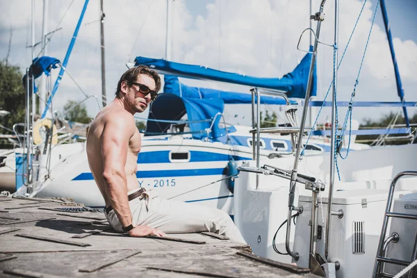 Sexy bearded man standing on the yacht club. Guy on a sailing boat. Handsome man enjoying life, traveling on yacht along beautiful Europe, guy with fit sexy body modeling, summer vacation