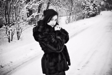 Ayrıca retro görünümlü hoş bir bayan kışın yürüyüş tarzında doğal kürk manto giymiyor. Kadının keyfi yerinde. Kış tatili, siyah beyaz fotoğraf