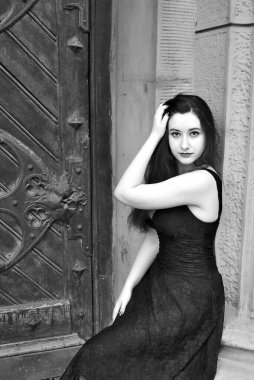Sonbaharda uzun saçlı gotik genç bir kadın. En eski Avrupa kilisesinin etrafında siyah elbiseli, klasik aksesuarlı.