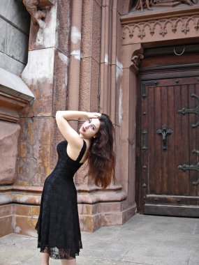 Sonbaharda uzun saçlı gotik genç bir kadın. En eski Avrupa kilisesinin etrafında siyah elbiseli, klasik aksesuarlı.