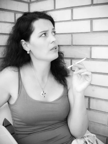 The harmful effect of nicotine on women\'s health and appearance. A middle-aged woman with a cigarette sits on the balcony and smokes. Harm from harmful habits