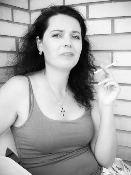 尼古丁对妇女健康和外表的有害影响 一个拿着香烟的中年妇女坐在阳台上抽烟 有害的习惯 — 图库照片