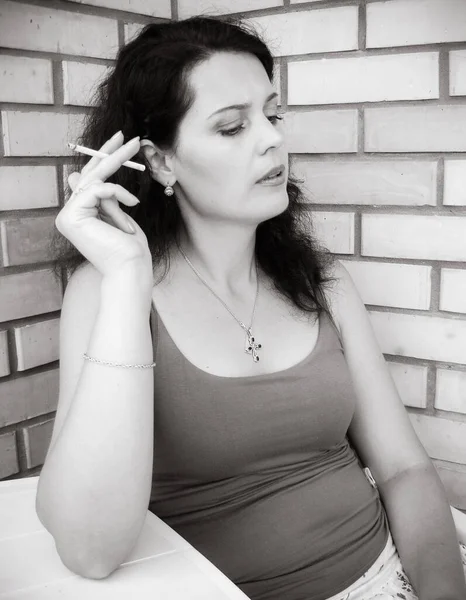 The harmful effect of nicotine on women\'s health and appearance. A middle-aged woman with a cigarette sits on the balcony and smokes. Harm from harmful habits