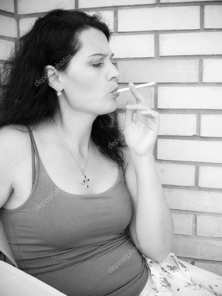 The harmful effect of nicotine on women's health and appearance. A middle-aged woman with a cigarette sits on the balcony and smokes. Harm from harmful habits