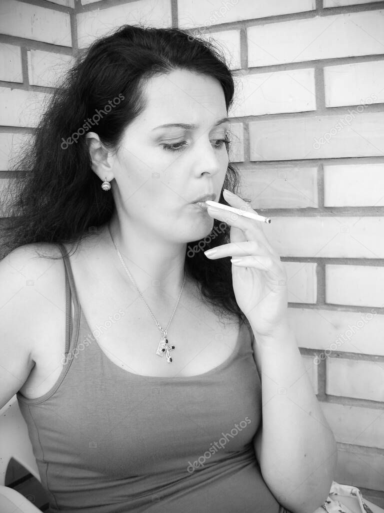 The harmful effect of nicotine on women's health and appearance. A middle-aged woman with a cigarette sits on the balcony and smokes. Harm from harmful habits