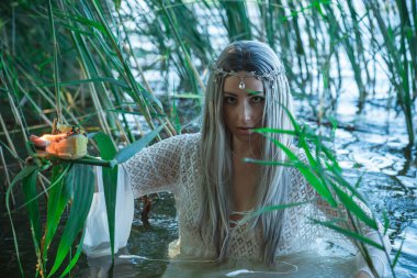 Gölde beyaz elbiseli deniz kızı gelini. Fantezi kızı. Gizemli bir sahne. Cadı nehirde duruyor ve büyü yapıyor. Peri masalı