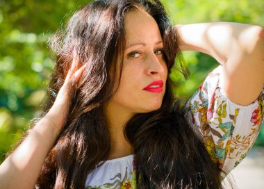 Avrupa görünümlü, yaz elbisesi içinde uzun siyah saçlı orta yaşlı bir kadın kentin parkında dinleniyor. Kompleksleri olmayan biraz kilolu bir kadın