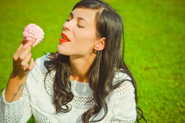 A young woman with dark hair in a white sweater at a picnic is resting on the green grass and is having a rest this afternoon. Beauty of nature and relax at sunny day