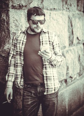 Büyük bir metropolün sakini olan bir adam, sağlıksız bir hayat sürüyor, yerel bir barın yakınında duruyor ve sigara içiyor.