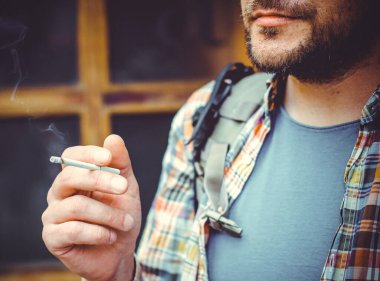 Büyük bir metropolün sakini olan bir adam, sağlıksız bir hayat sürüyor, yerel bir barın yakınında duruyor ve sigara içiyor.