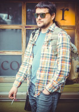 Büyük bir metropolün sakini olan bir adam, sağlıksız bir hayat sürüyor, yerel bir barın yakınında duruyor ve sigara içiyor.