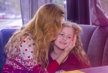 Açık hava restoranında sıcak çikolata içen sevimli, iri yarı bir kız. Annesiyle birlikte şehir kafesinde oturan neşeli küçük bir kızın portresi, iyi bir ruh hali, şık giyinmiş, eğleniyor, neşeli gülüyor.