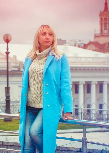 Attractive middle aged woman in blue coat walking in the city. Plus size Fashion woman portrait of trendy lady posing at the city in Europe street fashion