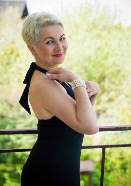 Kokteyl desenli elbise giymiş güzel Avrupalı olgun kadın işten sonra bir çiftlikte dinleniyor. Evde dinlen ve misafirleri bekle.