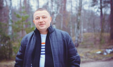 Soğuk bir günde, ormanda, sıcak kıyafetler içinde, orta yaşlı bir adamın portresi. Kış günü ağaçların arka planında siyah ceket giyen şık şık bir adam.