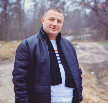 Soğuk bir günde, ormanda, sıcak kıyafetler içinde, orta yaşlı bir adamın portresi. Kış günü ağaçların arka planında siyah ceket giyen şık şık bir adam.