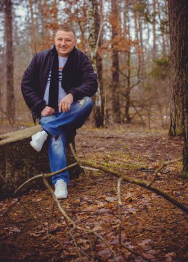 Soğuk bir günde, ormanda, sıcak kıyafetler içinde, orta yaşlı bir adamın portresi. Kış günü ağaçların arka planında siyah ceket giyen şık şık bir adam.