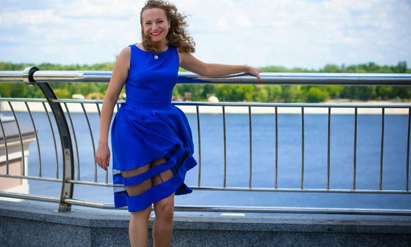 Blond hair curly woman plus size European appearance in blue retro dress walk in city at sunny warm day with good mood