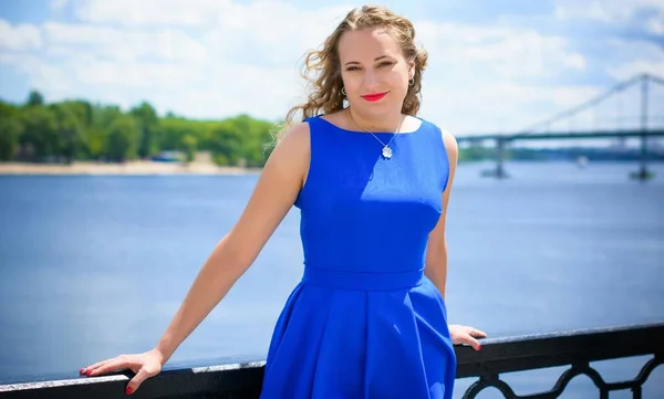 Blond hair curly woman plus size European appearance in blue retro dress walk in city at sunny warm day with good mood