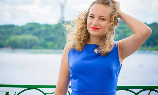 Blond hair curly woman plus size European appearance in blue retro dress walk in city at sunny warm day with good mood