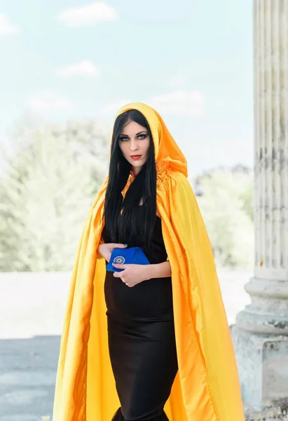 Mystical woman in yellow cloak, black dress, and tarot cards at old town, Halloween date, party outfit