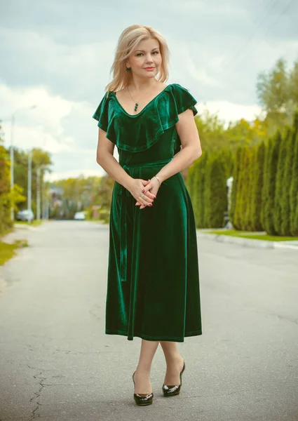 A middle-aged woman in a vintage green velvet dress and emerald accessories for a walk in a small cottage town. The concept of vintage and retro femininity