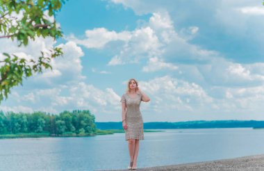 Güzel, sarışın, romantik, iri yarı, deniz kenarında şık, altın elbiseli bir kadın. Moda konsepti, şık kıyafetler.