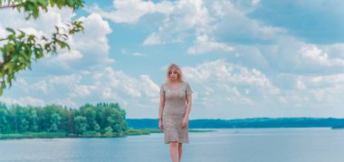 Güzel, sarışın, romantik, iri yarı, deniz kenarında şık, altın elbiseli bir kadın. Moda konsepti, şık kıyafetler.