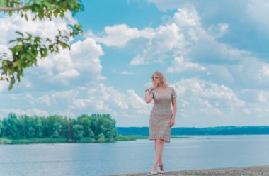 Güzel, sarışın, romantik, iri yarı, deniz kenarında şık, altın elbiseli bir kadın. Moda konsepti, şık kıyafetler.