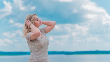 Güzel, sarışın, romantik, iri yarı, deniz kenarında şık, altın elbiseli bir kadın. Moda konsepti, şık kıyafetler.