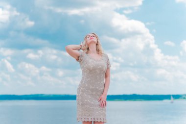 Güzel, sarışın, romantik, iri yarı, deniz kenarında şık, altın elbiseli bir kadın. Moda konsepti, şık kıyafetler.