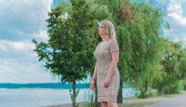 Güzel, sarışın, romantik, iri yarı, deniz kenarında şık, altın elbiseli bir kadın. Moda konsepti, şık kıyafetler.