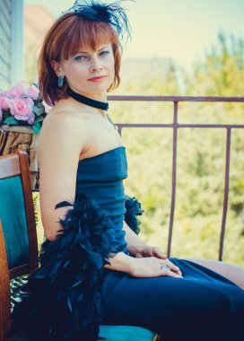 Siyah, eski moda uzun elbiseli, şık aksesuarlı, kolyeli, küpeli ve taşlı yüzüklü orta yaşlı güzel bir kadın. Siyah elbiseli kadın ve balkondaki boa