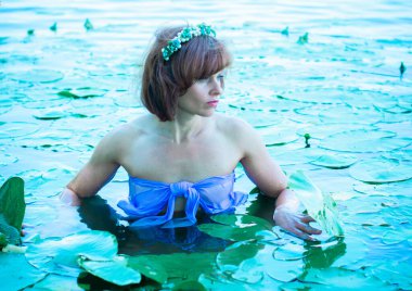 Bir kadın, sıcak bir yaz gününde, bir deniz kızına benzeyerek gölde banyo yapıyor. Nehirde romantik bir tarzda olgun bir kadın