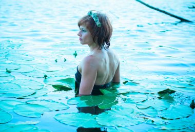 Bir kadın, sıcak bir yaz gününde, bir deniz kızına benzeyerek gölde banyo yapıyor. Nehirde romantik bir tarzda olgun bir kadın