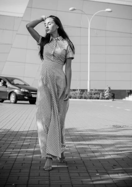 Beautiful young skinny girl walks around the city in a long dress in a cage and enjoys the day