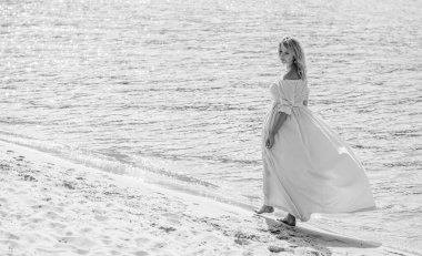 Orta yaşlı bir kadın, artı açık mavi elbiseli, bir şehir rıhtımında tatil gününde dinleniyor. Şehirde kadınlık ve romantizm kavramı