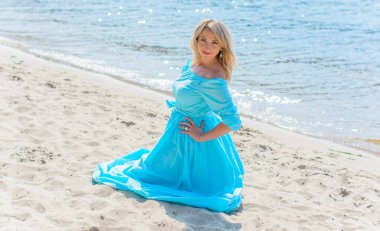 Orta yaşlı bir kadın, artı açık mavi elbiseli, bir şehir rıhtımında tatil gününde dinleniyor. Şehirde kadınlık ve romantizm kavramı