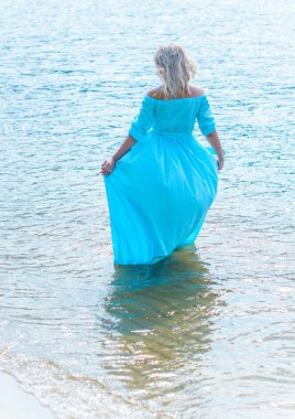 Orta yaşlı bir kadın, artı açık mavi elbiseli, bir şehir rıhtımında tatil gününde dinleniyor. Şehirde kadınlık ve romantizm kavramı 