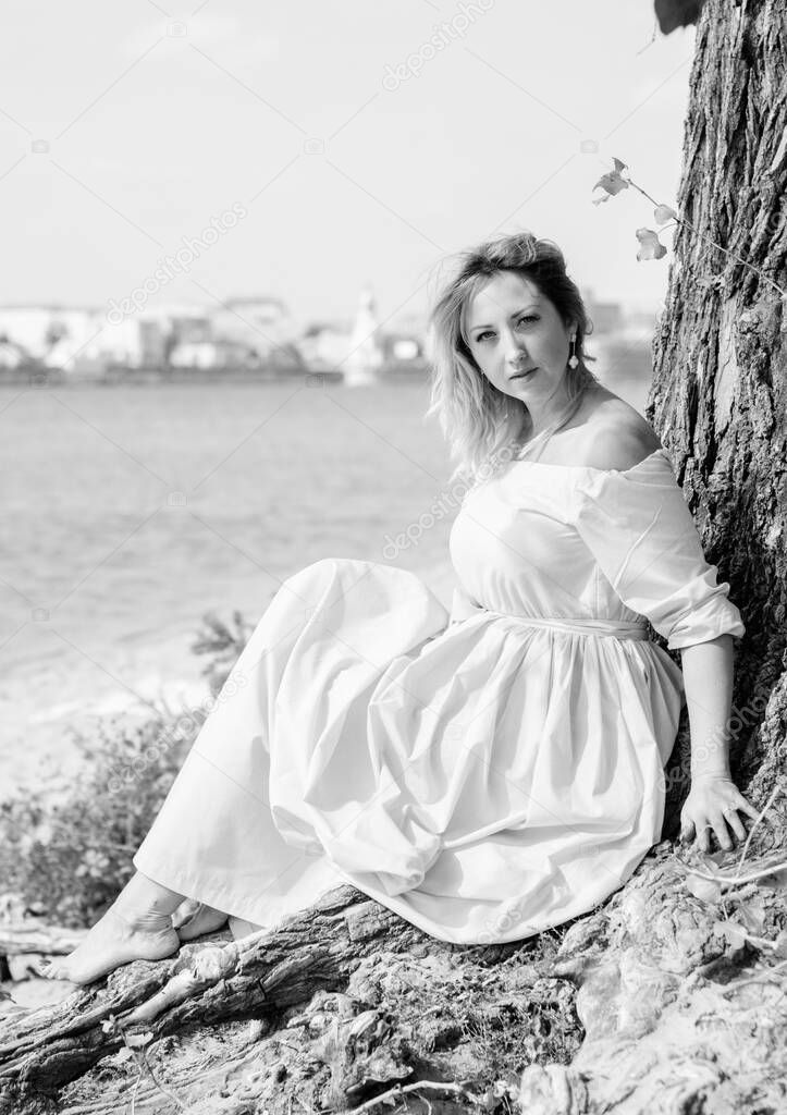 A middle-aged woman, plus in a light blue dress, rests on a city waterfront on a day off. The concept of femininity and romance in the city bustle