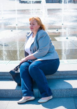 Mutlu kilolu kadın iyi gününde sokaklarda yürüyor. Boyut olarak güneşli bir portre artı bayan. Şehir caddesinde duran güzel şişman kadın.