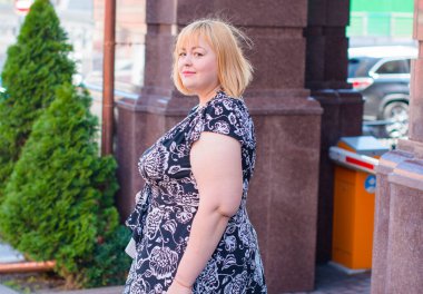 Happy overweight woman walking the city street at good day. Sunny portrait of size plus lady. Beautiful overweight woman standing on city street clipart