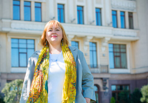 Счастливая женщина с избыточным весом гуляет по городской улице в добрый день. Солнечный портрет размера плюс дама. Красивая толстая женщина, стоящая на городской улице