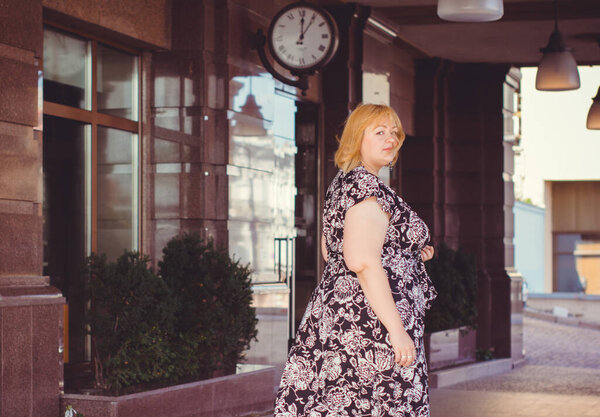 Счастливая женщина с избыточным весом гуляет по городской улице в добрый день. Солнечный портрет размера плюс дама. Красивая толстая женщина, стоящая на городской улице