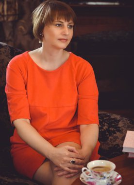 Yetişkin bir kadın bir odada oturur çay içer ve keyifli bir şekilde büyüleyici bir kitap okur.