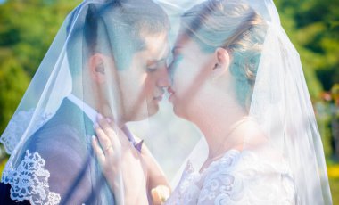 Düğün sonrası mutlu gelin ve damat. Damat gelinden daha genç. Düğün çifti, parkta yeni evliler öpüşüyor.