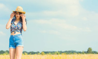 Parlak makyajlı, güzel seksi bir kadın Amerikan tarzı, saman şapka ve kot şortuyla altın bir arka plan gökyüzünde.